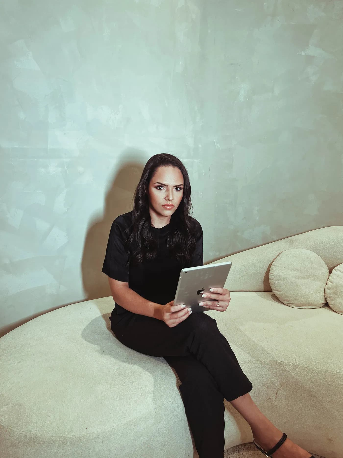 Daniele Santos sentada em um sofá claro, com um tablet nas mãos